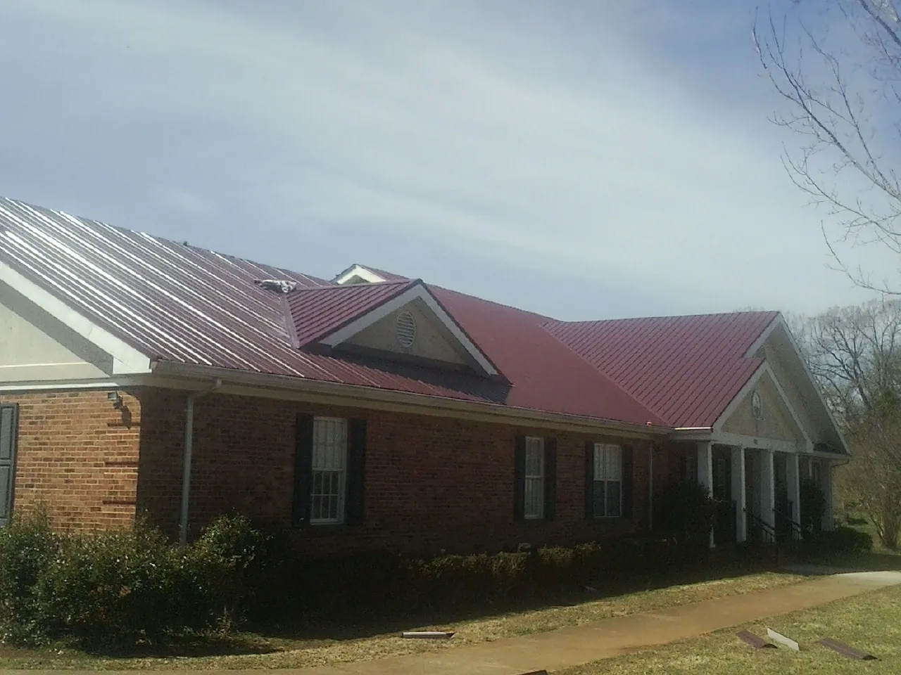 Red metal roof with gabled entries on a long brick building, from a Hail Damage Roof Repair job in Danciger