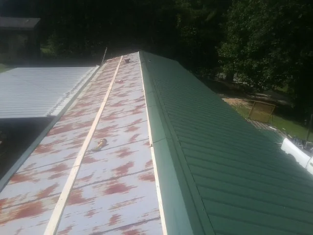Old rusted panels beside newly installed green metal roofing — Wind Damage Roof Repair by Roofing Brothers in Danciger