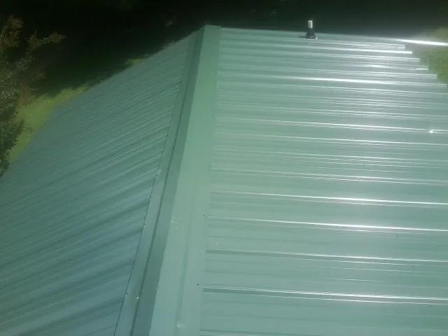 New green metal panels meeting at the ridge of a roof — Flat Roof Repair work by our crew in Danciger