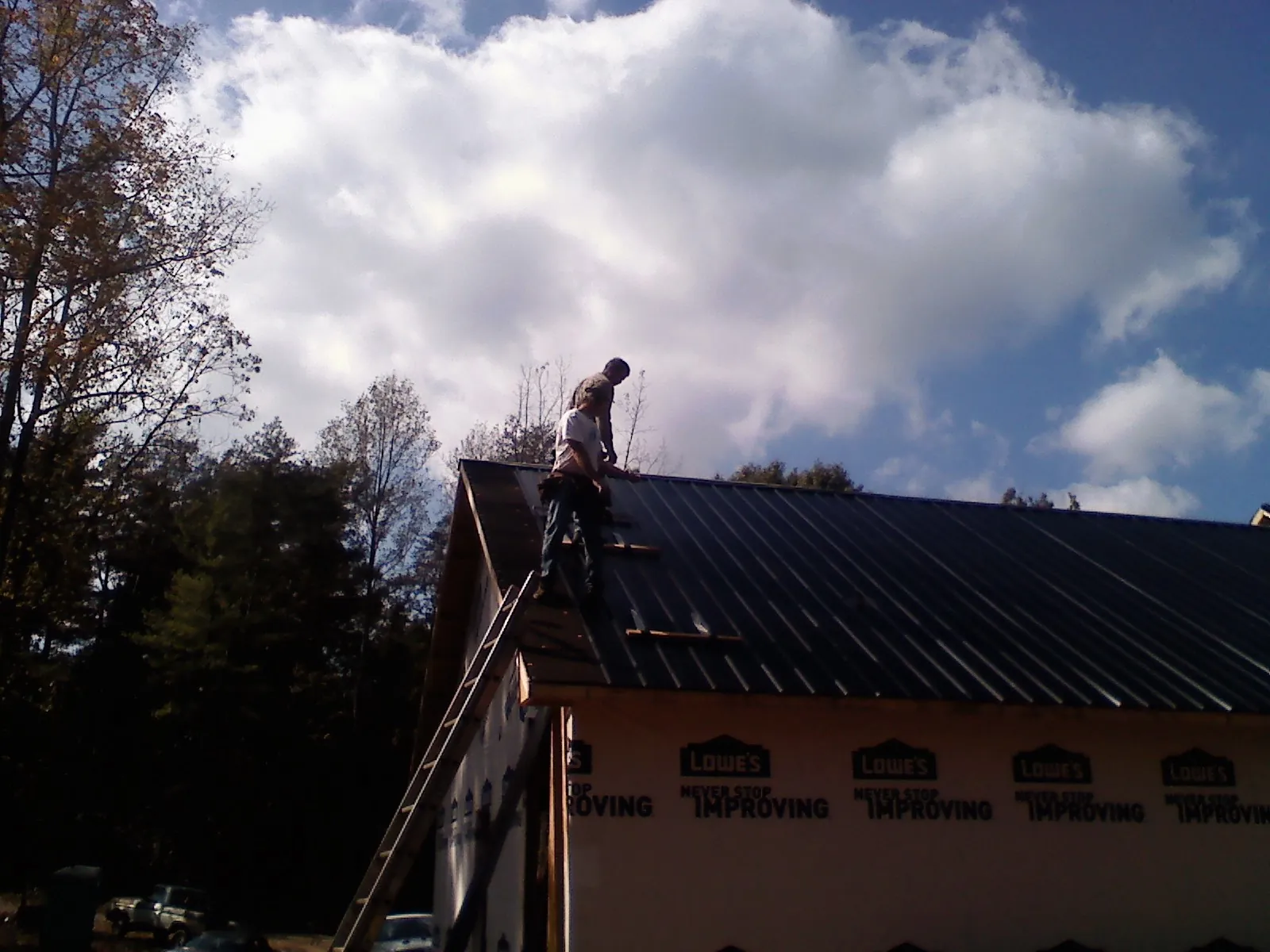 Roofer fastening dark metal panels high against a cloudy sky, from a Roof Inspection job in Danciger