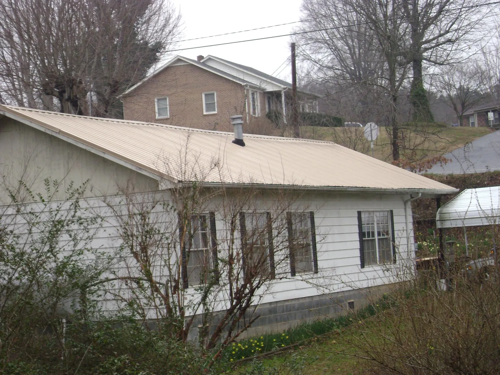 Tan metal roof on a white sided house set into a hillside — Commercial Roofing by Roofing Brothers in Danciger